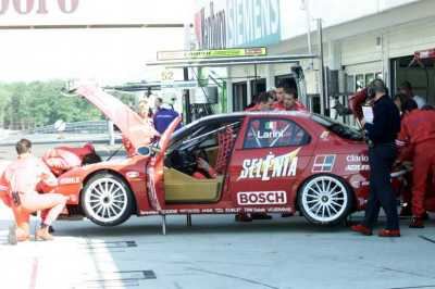 Pilota in tuta da gara accanto all'Alfa Romeo 156.